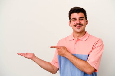 Beyaz arka planda izole edilmiş genç beyaz bir adam, palmiye üzerinde bir fotokopi alanı tutarken heyecanlı..