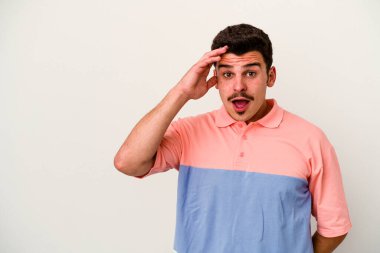 Beyaz arka planda izole edilmiş genç beyaz bir adam uzaklara bakıyor ve elini alnına koyuyor..