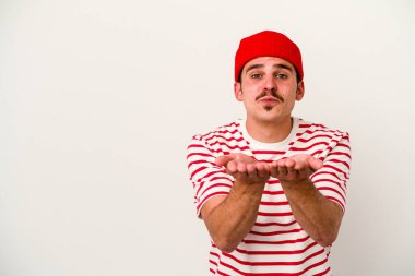 Beyaz arka planda izole edilmiş genç beyaz bir adam dudaklarını katlıyor ve hava öpücüğü vermek için avuç içleri tutuyor..