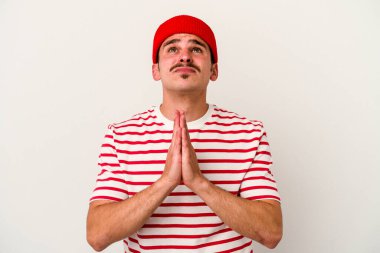 Beyaz arka planda izole edilmiş genç beyaz bir adam el ele tutuşup, ağız kenarında dua ediyor, kendinden emin..