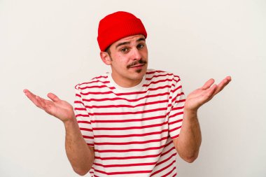 Beyaz arka planda izole edilmiş genç beyaz bir adam sorgulama sırasında omuz silkiyor ve şüphe duyuyor..