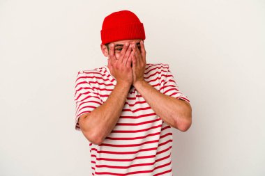 Beyaz arka planda izole edilmiş genç beyaz bir adam kameraya parmaklarıyla göz kırpıyor, yüzünü kapatmaktan utanıyor..