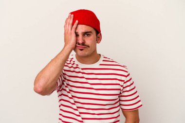 Beyaz arka planda izole edilmiş genç beyaz bir adam yorgun ve uykulu bir şekilde elini başının üstünde tutuyor..