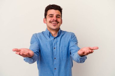 Beyaz arka planda izole genç beyaz adam kollarıyla ölçek yapar, mutlu ve kendinden emin hisseder..