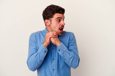 Beyaz arka planda izole edilmiş genç beyaz bir adam şans için dua ediyor, şaşırmış ve ağzını açıp önüne bakıyor..