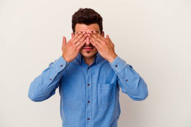 Beyaz arka planda izole edilmiş genç beyaz bir adam elleriyle gözlerini kapatmaktan korkuyor..