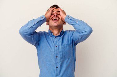 Beyaz arka planda izole olmuş genç beyaz bir adam ellerini başının üstünde tutarak neşeyle gülüyor. Mutluluk kavramı.