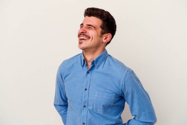 Beyaz arka planda izole edilmiş genç beyaz adam gevşemiş ve mutlu bir şekilde gülüyor, boynunda dişlerini gösteriyor..