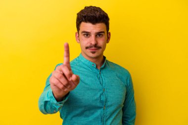 Sarı arka planda izole genç beyaz adam parmak ile bir numara gösteriyor.