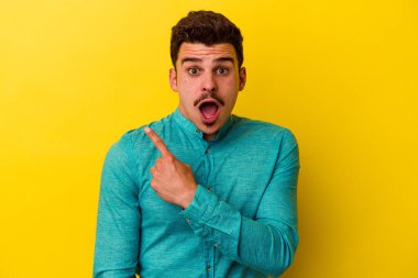 Sarı arka planda izole edilmiş genç beyaz adam yan tarafı işaret ediyor.