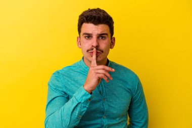 Sarı arka planda izole edilmiş genç beyaz bir adam ya sır saklıyor ya da sessizlik istiyor..