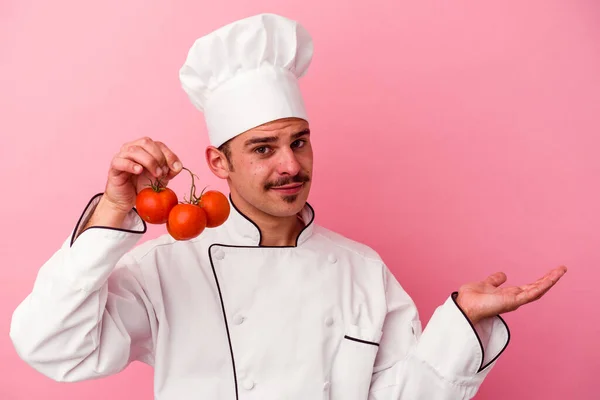 Mladý Kavkazský Kuchař Muž Drží Rajčata Izolované Růžovém Pozadí Ukazující — Stock fotografie