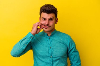 Sarı arka planda izole edilmiş genç beyaz bir adam parmakları dudaklarında bir sır saklıyor..