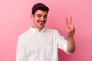 Pembe arka planda izole edilmiş genç beyaz adam zafer işareti gösteriyor ve gülümsüyor..