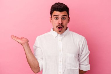 Pembe arka planda izole edilmiş genç beyaz adam, avuç içi fotokopi alanını elinde tutmaktan etkilenmiş..