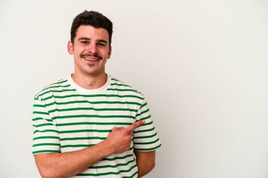 Beyaz arka planda izole edilmiş genç beyaz bir adam gülümsüyor ve boş alanda bir şeyler gösteriyor..