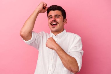 Pembe arka planda soyutlanmış genç beyaz adam özel bir günü kutluyor, atlıyor ve enerjiyle kollarını kaldırıyor..