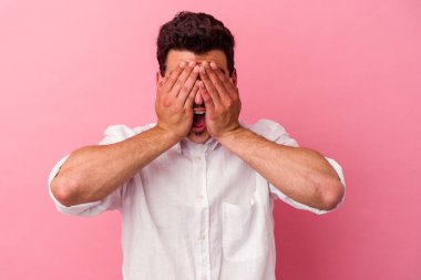 Pembe arka planda soyutlanmış genç beyaz adam elleriyle gözlerini kapatıyor, geniş bir gülümsemeyle bir sürpriz bekliyor..