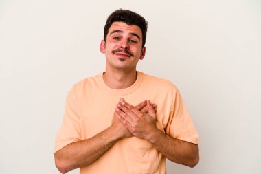 Beyaz arka planda soyutlanmış beyaz tenli genç bir adam gülüyor, elini yüreğine koyuyor, mutluluk kavramını koruyor..