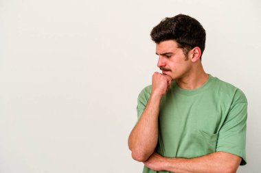 Beyaz arka planda izole edilmiş genç beyaz bir adam şüpheli ve şüpheci bir ifadeyle yana bakıyor..