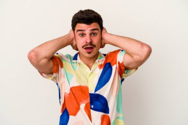 Beyaz arka planda izole edilmiş genç beyaz bir adam kulakları kulaklarıyla kapatıyor ve çok ses duymamaya çalışıyor..