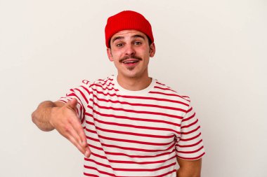 Beyaz arka planda izole edilmiş genç beyaz bir adam selamlama jesti olarak kameraya elini uzatıyor..