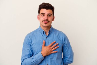 Beyaz arka planda izole edilmiş genç beyaz adam yemin ediyor, elini göğsüne koyuyor..