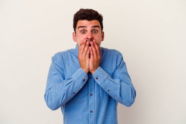 Beyaz arka planda izole edilmiş genç beyaz adam şok olmuş, ağzı ellerle kaplanmış, yeni bir şey keşfetmeye hevesli..