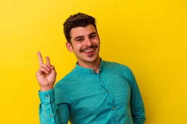 Sarı arka planda izole edilmiş genç beyaz adam neşeli ve kaygısız parmakları olan bir barış sembolü gösteriyor..