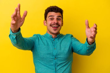 Sarı arka planda izole genç beyaz adam hoş bir sürpriz alıyor, heyecanlı ve el kaldırıyor..