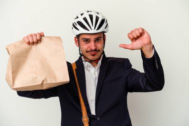 Bisiklet kaskı takan ve elinde tuttuğu beyaz arka planda izole edilmiş yiyecekleri alan genç beyaz bir adam gururlu ve kendinden emin hissediyor, örnek olarak.