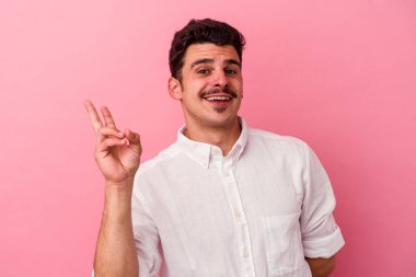 Genç beyaz adam pembe arka planda izole edilmiş neşeli ve kaygısız parmakları olan bir barış sembolü gösteriyor..