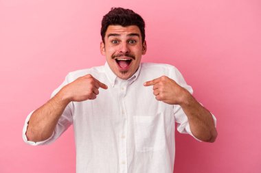 Pembe arka planda izole edilmiş genç beyaz adam parmağını göstererek şaşırdı, geniş bir gülümsemeyle..