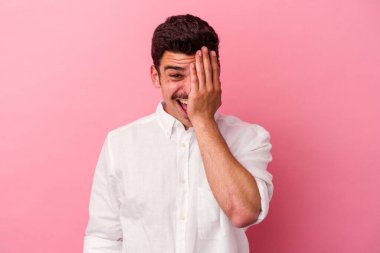 Pembe arka planda izole edilmiş genç beyaz adam yüzünün yarısını palmiye ile örterek eğleniyor..