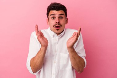 Pembe arka planda izole edilmiş genç beyaz adam şaşırdı ve şok oldu..