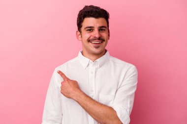Pembe arka planda izole edilmiş genç beyaz adam gülümsüyor ve boş alanda bir şeyler gösteriyor..