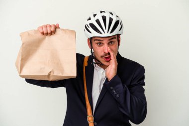 Bisiklet kaskı takan ve elinde beyaz arka planda izole edilmiş yiyeceklerle gezen genç beyaz iş adamı gizli bir sıcak fren haberinin olduğunu söylüyor.