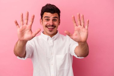 Pembe arka planda izole edilmiş genç beyaz adam on numarayı elleriyle gösteriyor..