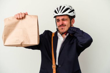 Bisiklet kaskı takan ve elinde tuttuğu beyaz arka planda izole edilmiş yiyecekleri alan kafasının arkasına dokunan, düşünen ve bir seçim yapan genç beyaz iş adamı..