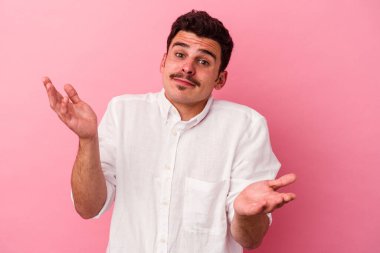 Pembe arka planda soyutlanmış genç beyaz bir adam sorgulama sırasında omuz silkiyor ve şüphe duyuyor..