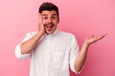 Pembe arka planda izole edilmiş genç beyaz bir adam avucunun içinde fotokopi alanı tutuyor, el üstünde tutuyor. Şaşırmış ve mutlu..