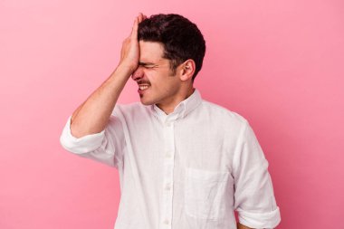 Pembe arka planda izole edilmiş genç beyaz bir adam bir şeyi unutuyor. Alnına avuç içi ve gözlerini kapatarak vuruyor..
