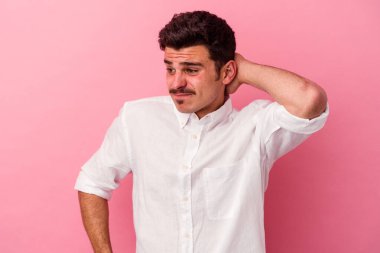 Kafkasyalı genç bir adam pembe arka planda izole edilmiş kafasının arkasına dokunuyor, düşünüyor ve bir seçim yapıyor..