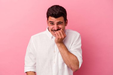 Pembe arka planda izole edilmiş, tırnak yiyen, gergin ve endişeli genç bir beyaz adam..