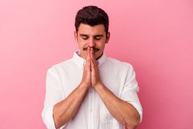 Pembe arka planda izole edilmiş genç beyaz bir adam. El ele tutuşup, ağız kenarında dua ediyor. Kendine güveniyor..