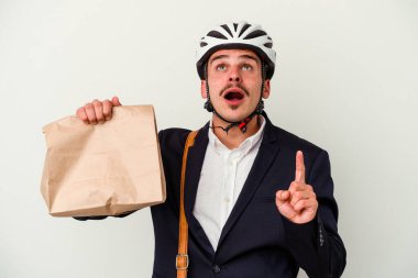 Bisiklet kaskı takan ve elinde tuttuğu beyaz arka planda izole edilmiş yiyecekleri alıp ağzı açık bir şekilde üst tarafı gösteren beyaz iş adamı..
