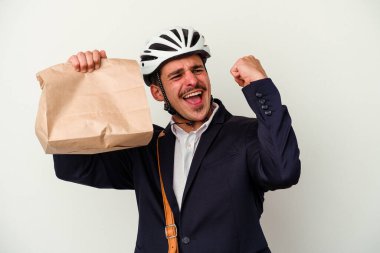 Bisiklet kaskı takan ve elinde tuttuğu genç beyaz arka planda izole edilmiş yiyecekleri alan beyaz bir adam zaferden sonra yumruğunu kaldırıyor..