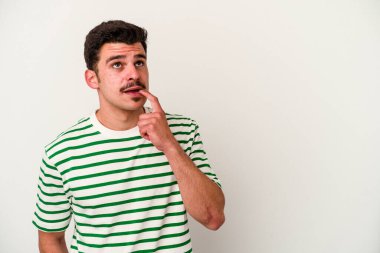 Beyaz arka planda izole edilmiş genç beyaz bir adam şüpheli ve şüpheci bir ifadeyle yana bakıyor..