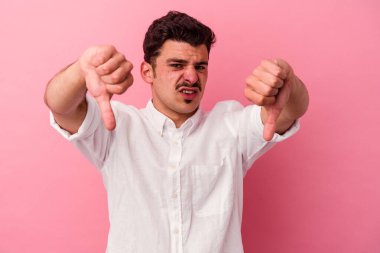Pembe arka planda izole edilmiş genç beyaz adam baş parmağını aşağı gösteriyor ve hoşlanmadığını ifade ediyor..
