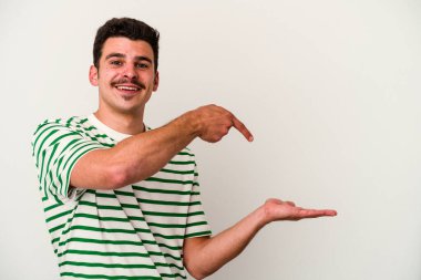 Beyaz arka planda izole edilmiş genç beyaz bir adam, palmiye üzerinde bir fotokopi alanı tutarken heyecanlı..